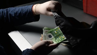 Hände nehmen Geldscheine aus einer Tasche.
