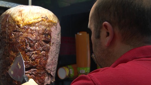 Ein Mitarbeiter in einem Döner-Imbiss schneidet Dönerfleisch an einem Spieß.