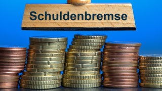 Über mehreren Münzstapeln schwebt ein Stempel mit der Aufschrift "Schuldenbremse"