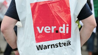 Ein Mensch trägt eine Weste mit der Aufschrift "Warnstreik".