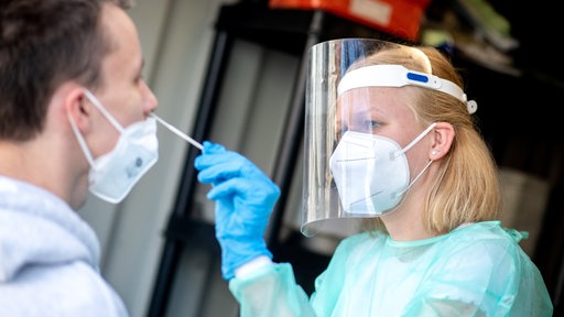 Eine Frau mit Gesichtsmaske und Mundschutz macht einen NAsenabstrich bei einem Mann