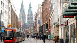 Passanten laufen durch die Bremer Innenstadt. Auf den Schienen der Obernstraße fährt eine Straßenbahn.