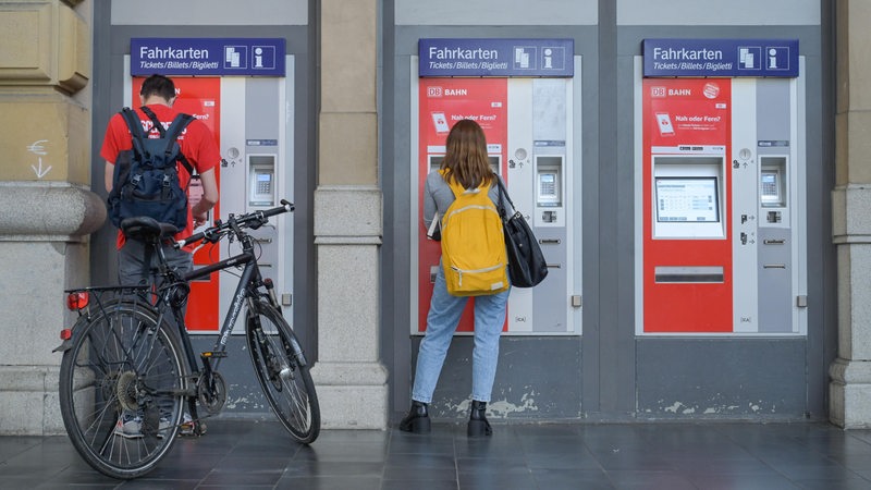 Zwei Personen stehen vor Fahrkartenautomaten.