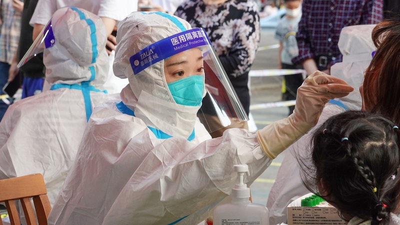 Eine chinesische Frau im Schutzanzug führt bei einer Landsfrau einen Corona-Test durch.