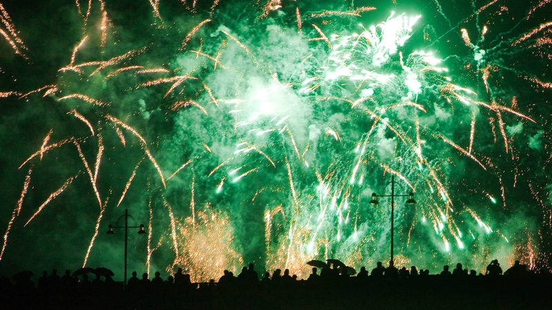 Menschen stehen zusammen und betrachten ein Feuerwerk in grüner Farbe.