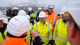 Eine Personengruppe steht an einem Pier. Alle tragen weiße Helme.