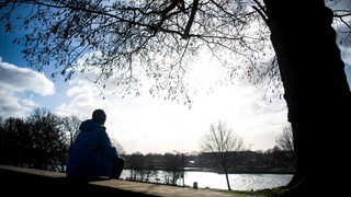 Ein Passant sitzt bei Sonnenschein am Ufer der Weser.