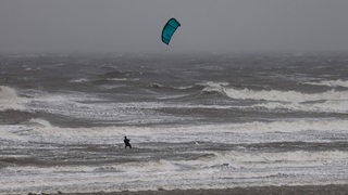 Ein Kitesurfer nutzt die Orkanböen für ein Rennen auf dem Wasser.