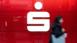 Eine Frau läuft am Logo der Sparkasse vorbei.