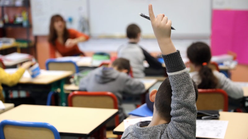 Junge sitzt im Klassenzimmer und zeigt auf