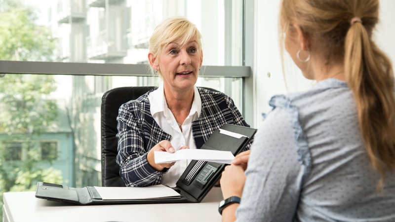 Eine Frau überreicht im Büro einer Bewerberin einen Arbeitsvertrag.