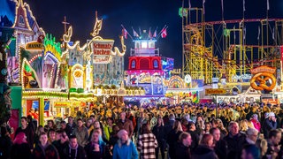 Die Fahrgeschäfte auf dem Freimarkt auf der Bürgerweide leuchten mit bunten Lichtern und Reklameschriftzügen.