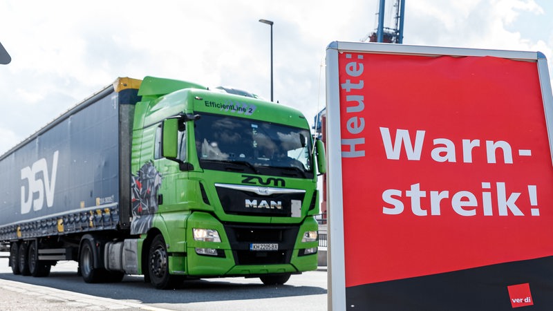 Ein Lkw fährt an einem Hafen hinter einem Schild mit der Aufschrift "Warnstreik!" vorbei.