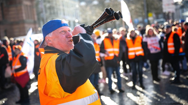 Ein Demonstrant steht mit einem Signalhorn vor Demonstranten der Eisenbahn- und Verkehrsgewerkschaft (EVG) mit Plakaten am Hauptbahnhof