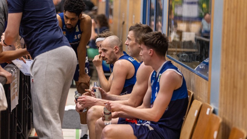 Basketball-Spieler der Eisbären Bremerhaven sitzen beim Timeout nachdenklich auf Stühlen.