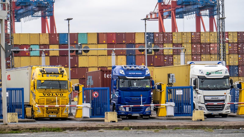 Drei Lkw stehen vor geschlossenen Schranken. Im Hintergrund sind Container zu sehen.