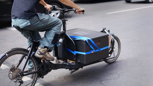 Ein Mann eine schwarze Kiste auf einem elektrischen Lastenfahrrad.