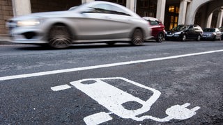 Ein Auto fährt an einem Symbol für ein Elektroauto vorbei. 