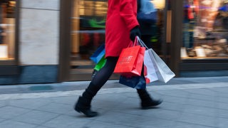 Frau mit Einkaufstüten läuft an einem Laden vorbei.