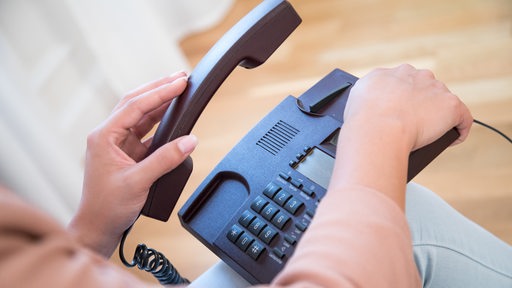 Eine Frau hält einen Telefonhörer in der Hand.