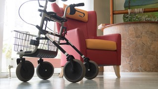 Ein Rollator steht vor einem leeren Sessel.