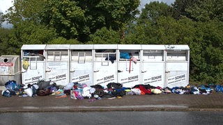 Vollgestopfte Altkleidercontainer stehen am Straßenrand.