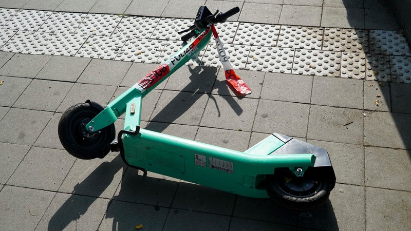 Ein E-Roller liegt auf dem Boden. An seinem Lenker ist ein rot-weißes Flatterband von der Polizei befestigt.