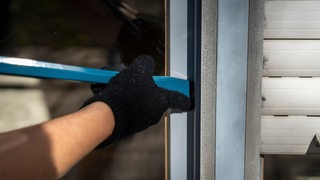 Ein Arm mit Handschuh hebelt mit einem Brecheisen ein Fenster auf