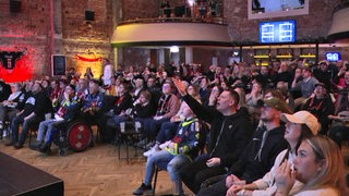 Eishockey-Fans der Fischtown Pinguins fiebern gemeinsam in einem ehemaligen Kino in Bremerhaven vor einer Leinwand beim Play-off-Spiel mit.