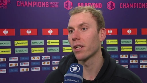 Eishockey-Torwart Maximilian Franzreb von den Fischtown Pinguins steht nach einem Champions-League-Spiel vor einer Werbewand beim Interview.