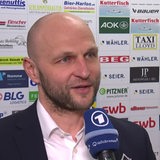 Eishockey-Manager Sebastian Furchner von den Fischtown Pinguins steht vor einer Werbewand beim Interview nach dem Sieg gegen Köln.