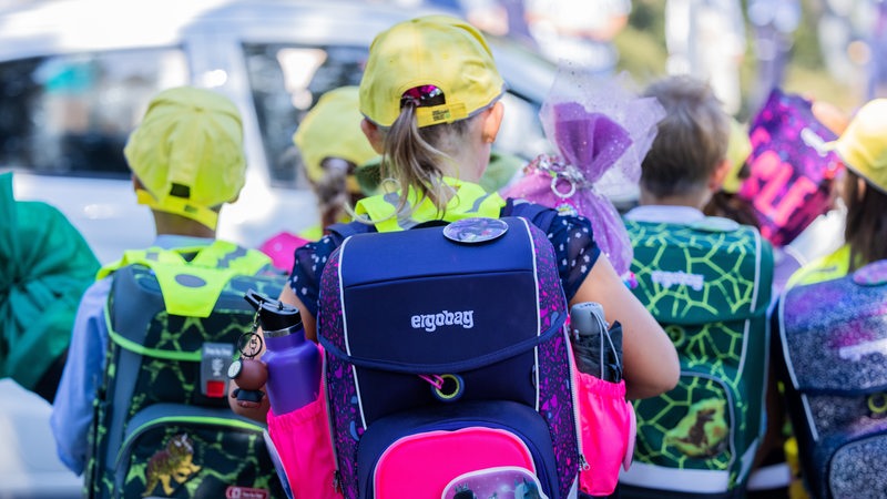 Mehrere Kinder mit Schulranzen und Cappies laufen eine Straße entlang, Schultüten in den Händen