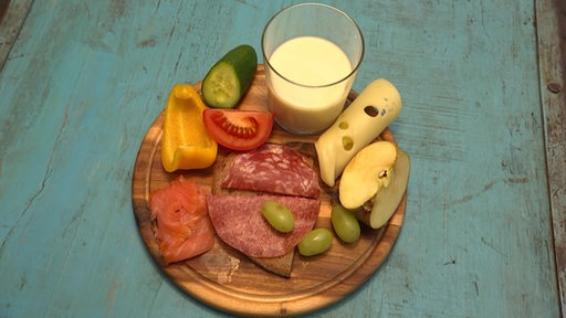 Ein Holzteller auf dem etwas Obst, Gemüse, Käse, Wurst und Milch angerichtet ist.