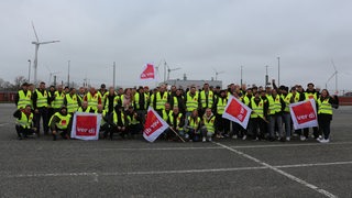 Menschen mit Warnwesten und Fahnen posieren auf einem Parkplatz für ein Gruppenfoto.