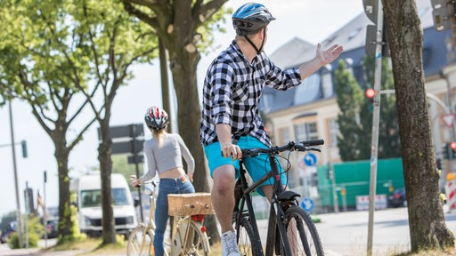 Ein Fahrradfahrer schaut nach hinten zu einer anderen Radfahrerin und macht eine Beschwerdegeste.