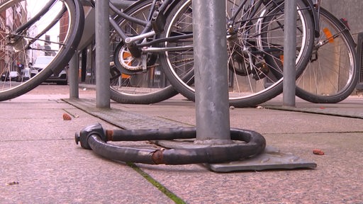 Ein aufgebrochenes Schloss am Fahrradständer mit Fahrrädern im Hintergrund.