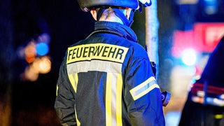 Ein Feuerwehrmann steht in Uniform an einem Einsatzort.