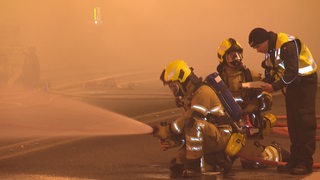 Einsatzleiter der Feuerwehrübung Mario Heuer im Interview, dahinter Feuerwehrmänner an einem Auto.