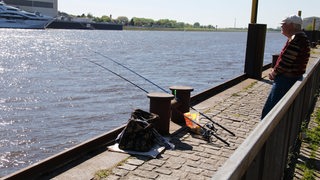 Mann steht mit Angel an der Weser