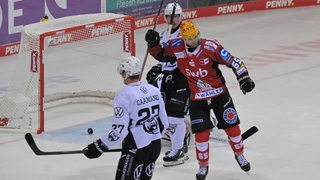 Drei Eishockeyspieler auf dem Spielfeld, einer von ihnen bejubelt ein Tor.