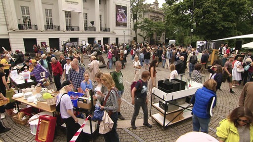 Auf dem Goetheplatz ist ein Flohmarkt mit vielen Menschen zu sehen. 