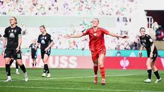 Werders Fußballerinnen stehen enttäuscht auf dem Rasen beim Pokal-Finale, als Bayern-Spielerin Lea Schüller mit ausgebreiteten Armen ihr Tor feiert.