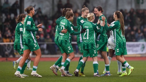 Die Fußballerinnen von Werder Bremen kommen auf dem Spielfeld jubelnd zusammen und klatschen sich nach einem Tor ab.