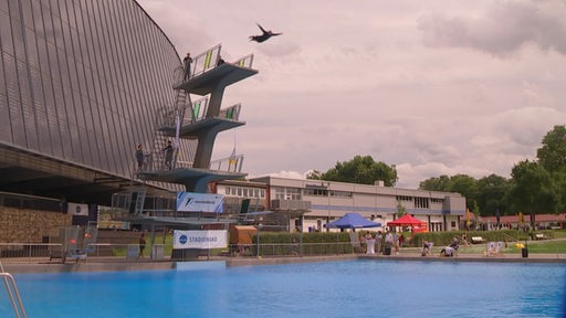 Zu sehen ist das Stadionbad und eine Person welche vom Springturm ins Wasser springt.