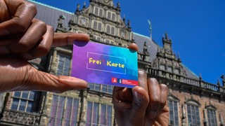 Eine Hand hält die Freikarte demonstrativ in die Kamera