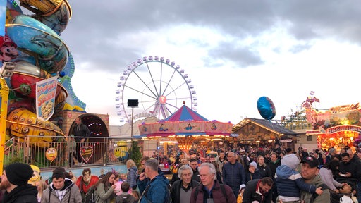 Das Riesenrad ist im Hintergrund zu sehen. Im Vordergrund laufen Besucher über den Freimarkt.