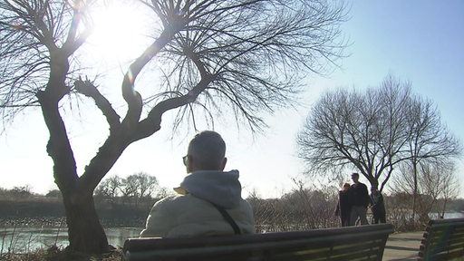 Spaziergänger gehen beim Sonnenschein entlang der Weser und sitzen auf einer Bank.