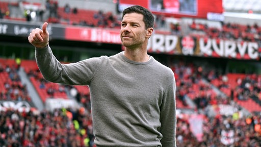 Xabi Alonso, Fußball-Trainer von Bayer Leverkusen, zeigt im Stadion lässig 'Daumen hoch' zu den Fans.