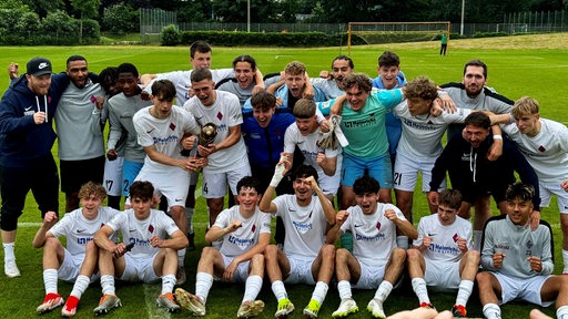 Die Fußballer des Blumenthaler SV posieren jubelnd mit ihrem Pokal beim Mannschaftsfoto.