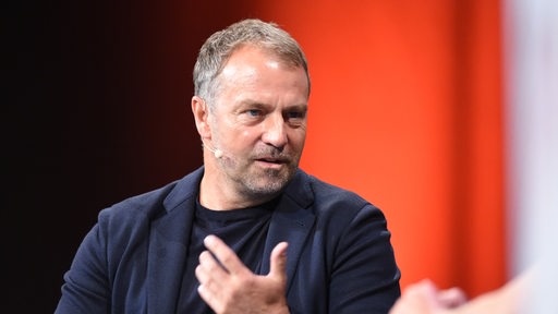 Hansi Flick sitzt auf dem Podium bei einer Diskussion.